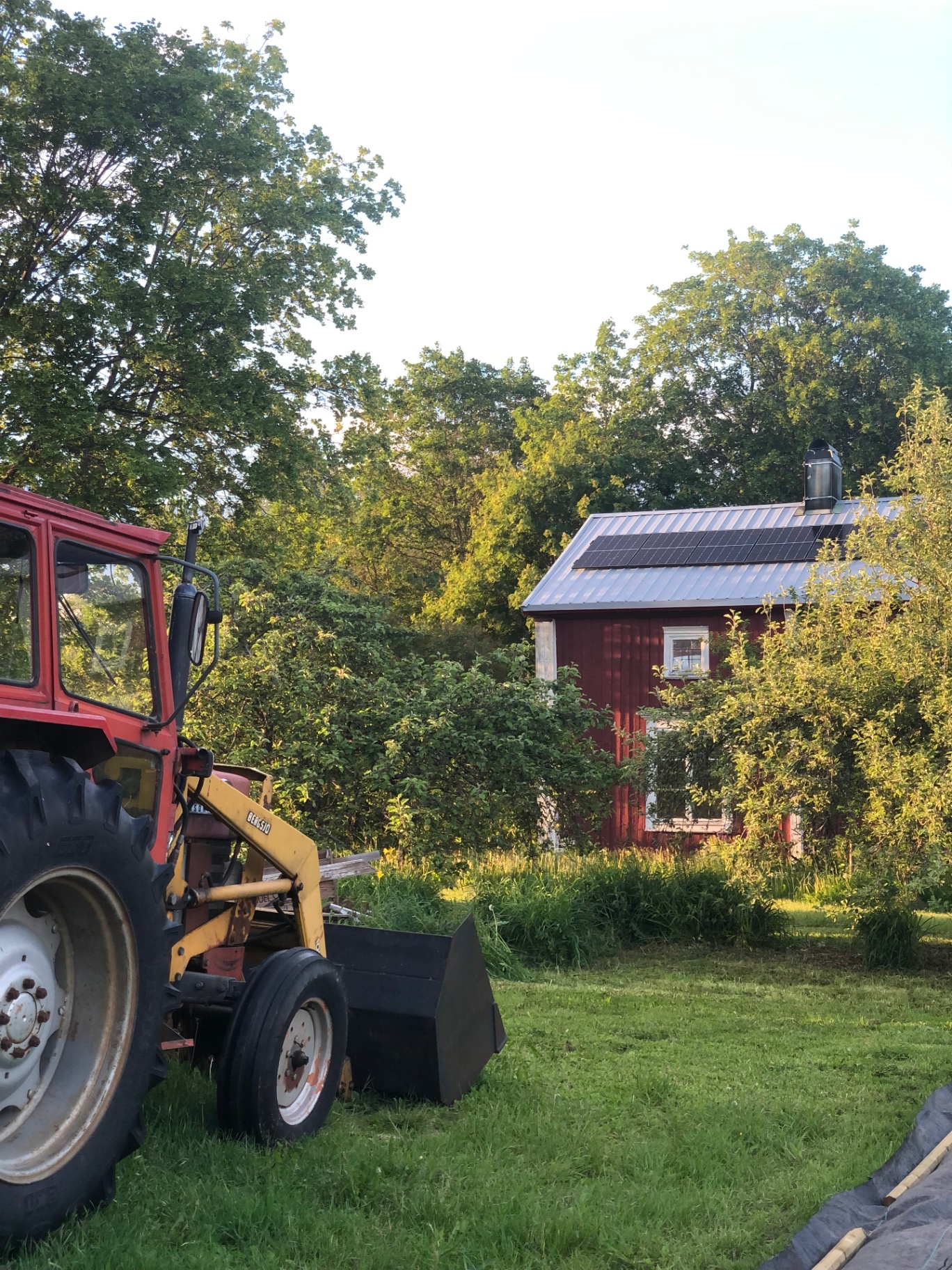 Karlgårds utomhusmiljö i sommarljus - gårdsplan, traktor och depåbyggnad.